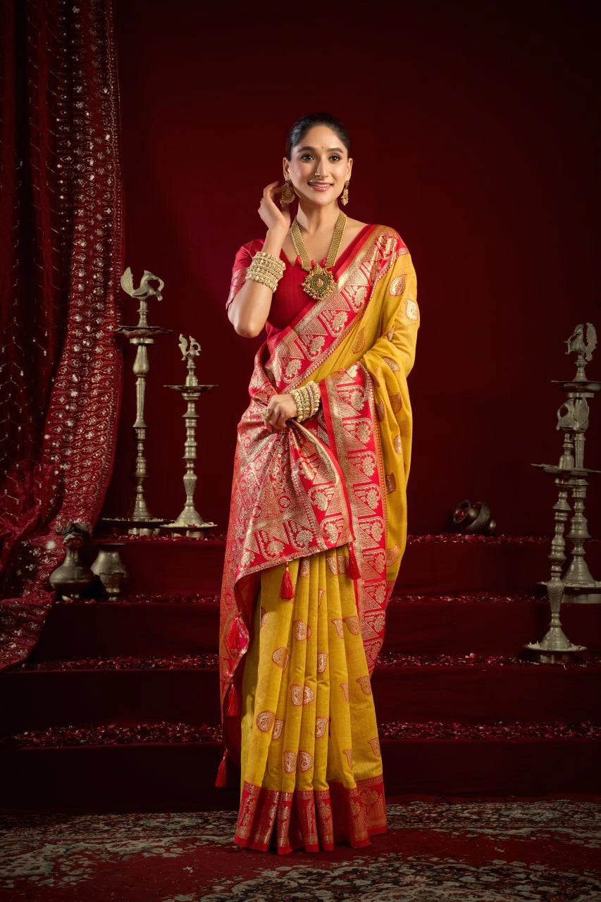 Woman in a yellow and red saree standing in a decorated room with red walls and decorative elements.
